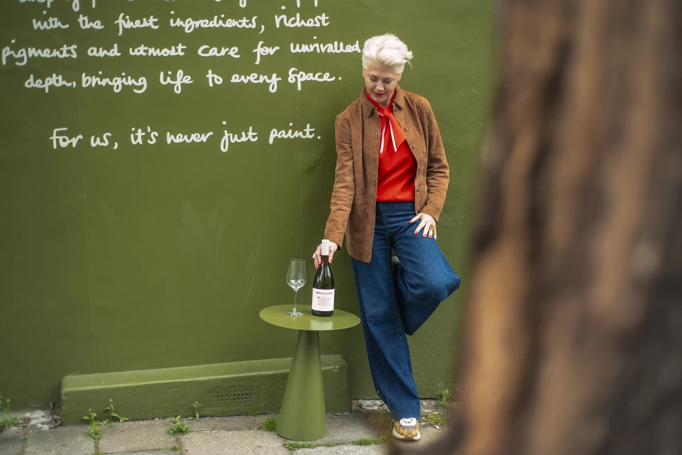 Person standing beside a bottle of Martín Códax wine and a wine glass against a green wall