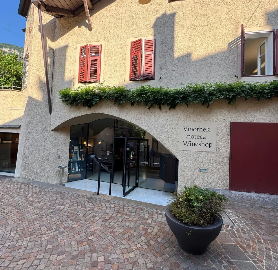 Traditional building with red shutters and an Alto Adige wine shop entrance on a cobbled street