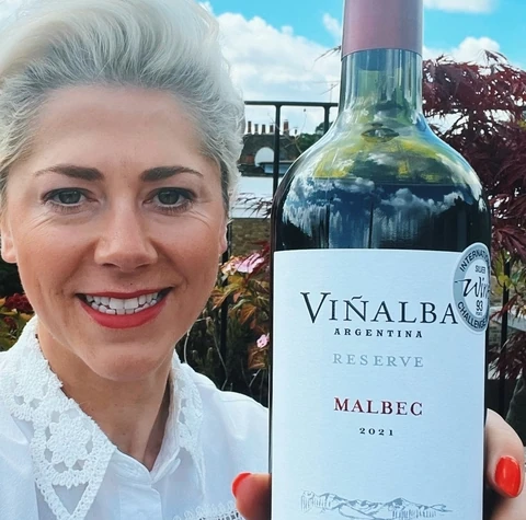A Viñalba Malbec Reserva bottle held outdoors beneath a bright blue sky