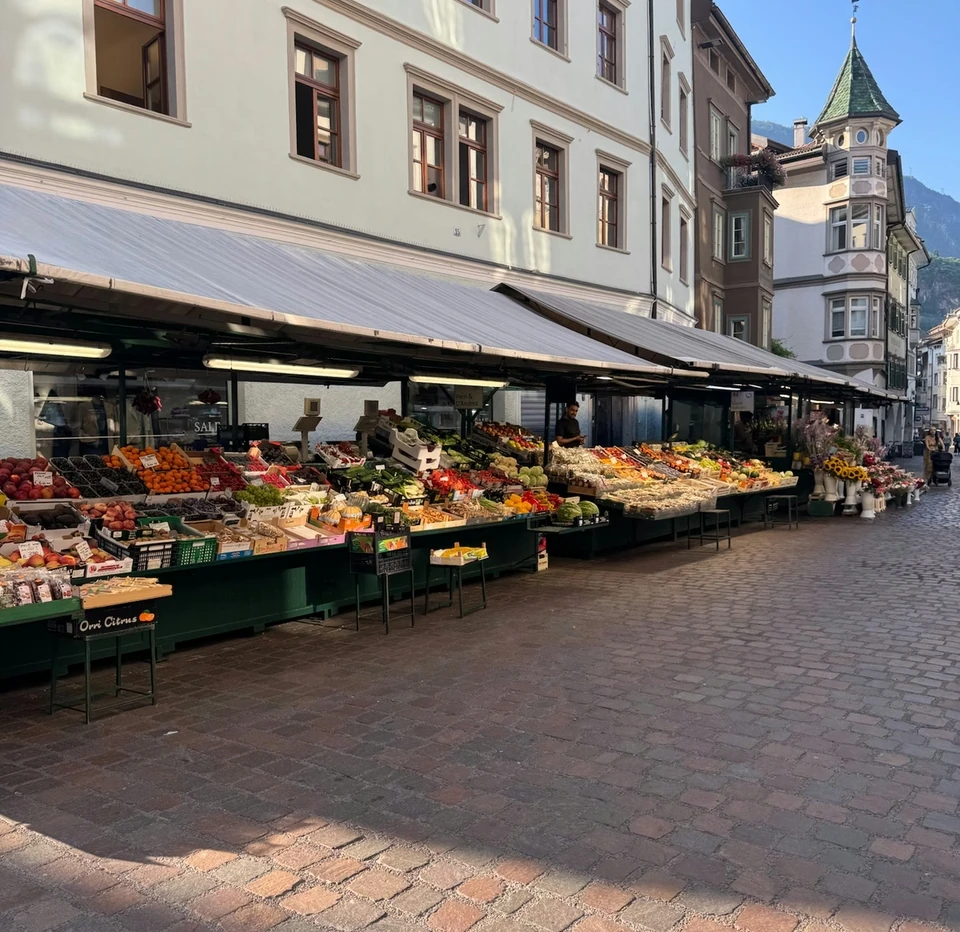 Open-air produce market on a cobbled street with historic buildings in Alto Adige