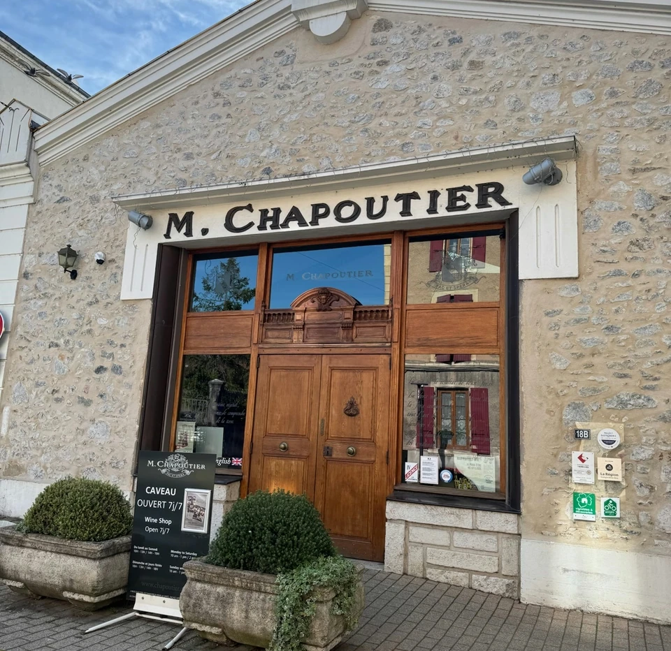 Stone-fronted M. Chapoutier wine shop with a wooden entrance and potted shrubs