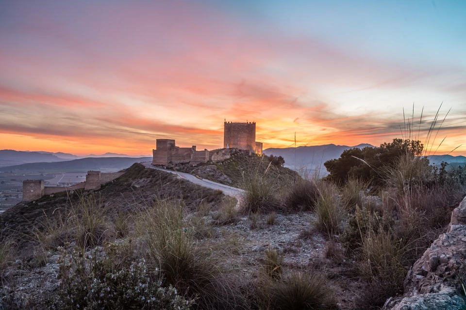 Castillo de Jumilla silhouetted against a vivid sunset over the surrounding hills