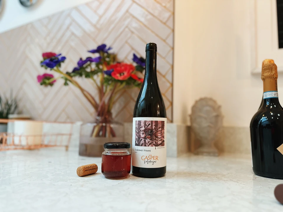 A bottle labelled Cabernet Franc beside a sparkling wine bottle, jar and loose cork on a kitchen worktop