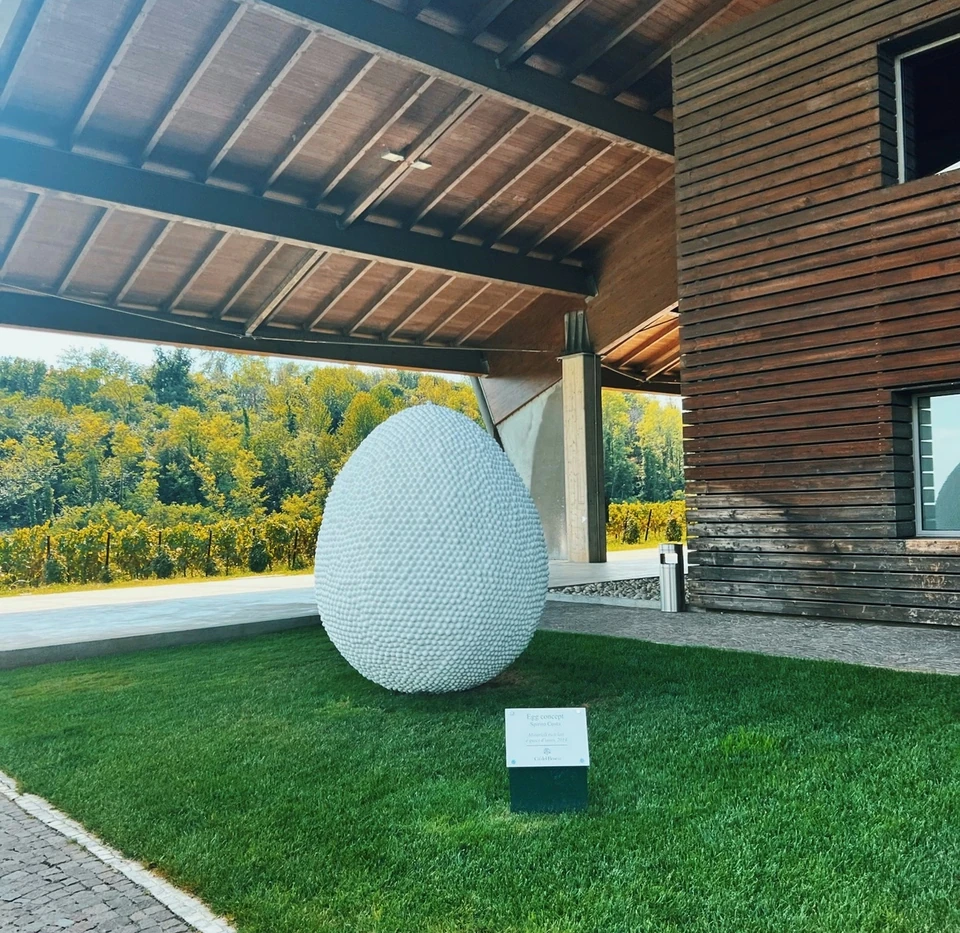 White textured egg sculpture outside a modern winery building beside a vineyard