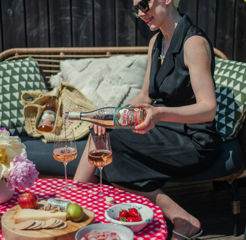 Woman pouring rosé at a garden picnic table with cheese, fruit and berries
