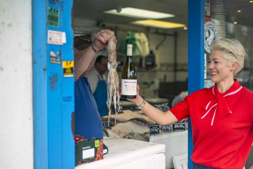 Woman in red holds a Martin Codax Albariño bottle beside a fishmonger displaying fresh octopus