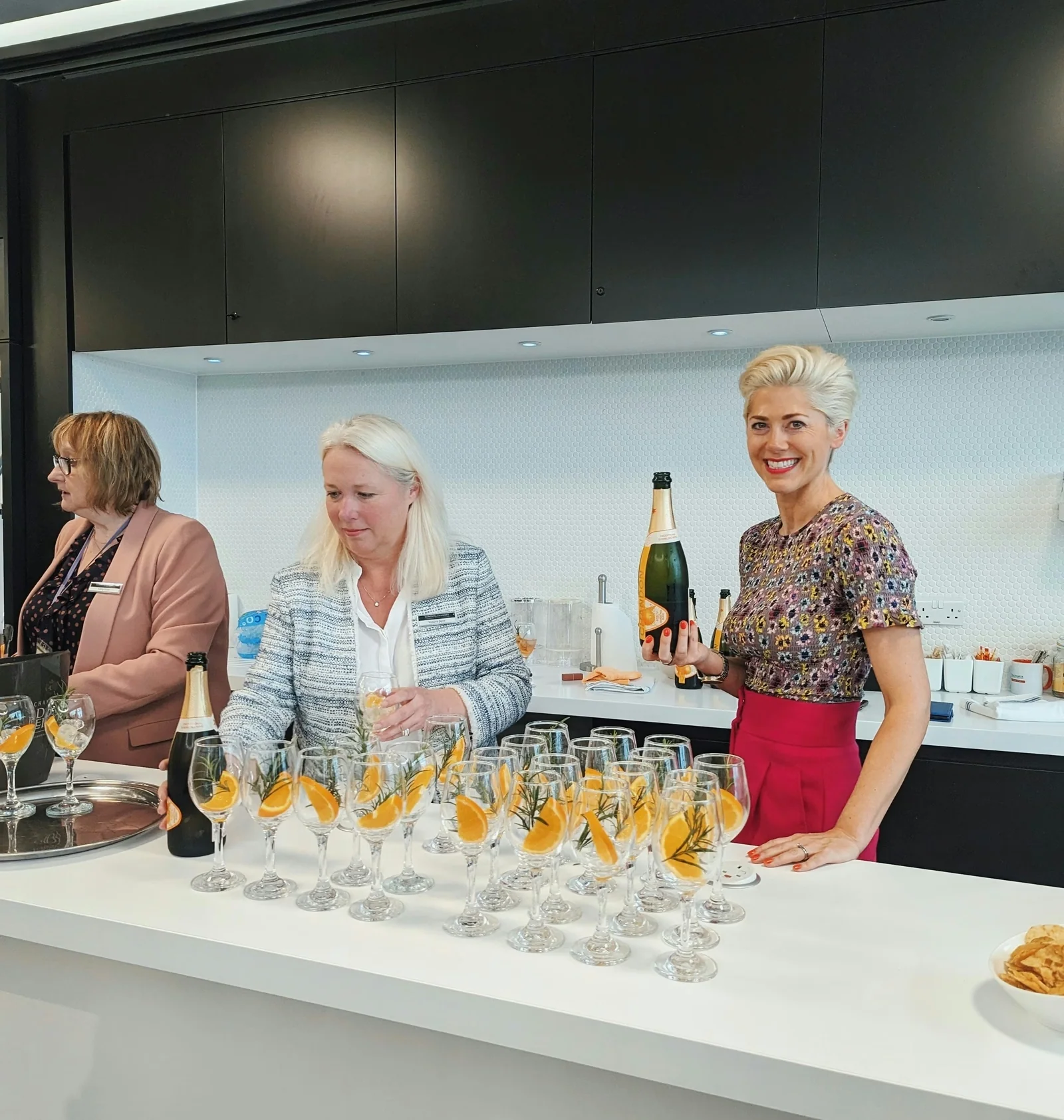 Three women prepare sparkling wine cocktails at a bar