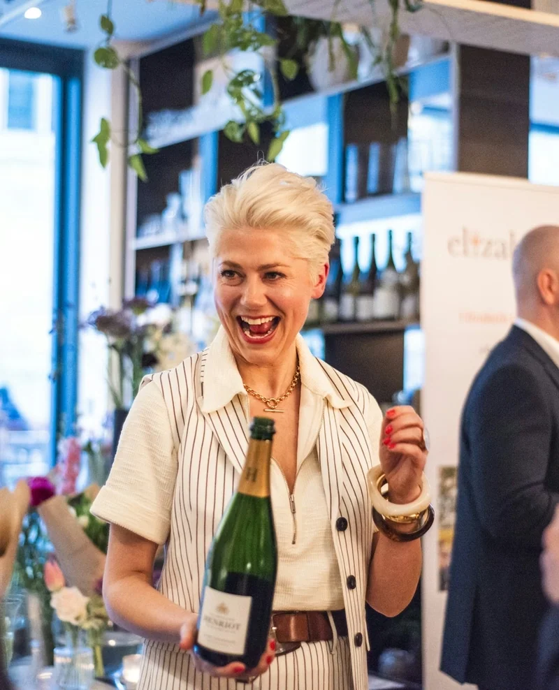 A woman holding a wine bottle at an indoor wine tasting