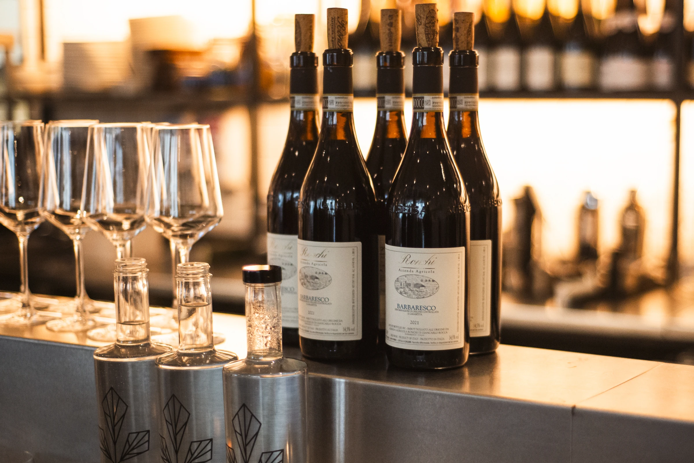 Stemware and bottles of Barbaresco lined up along a bar at golden hour